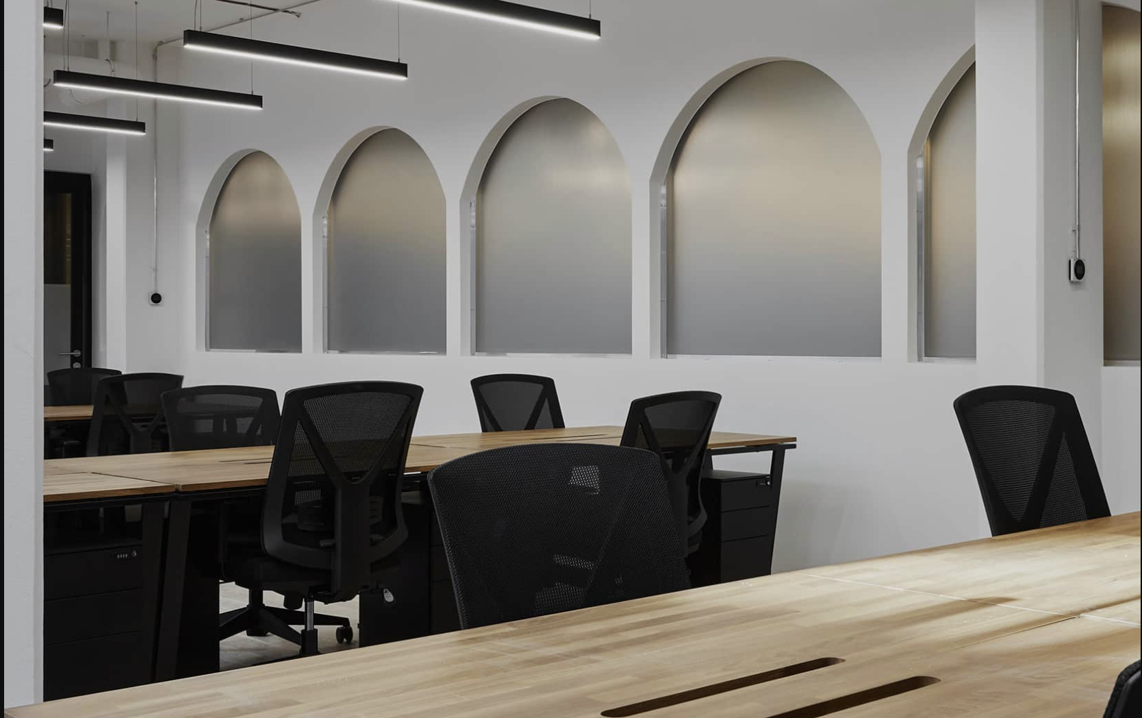 Modern Berlin office at Indy by Industrious Atrium Tower with wood desks, black mesh chairs and frosted arched wall niches