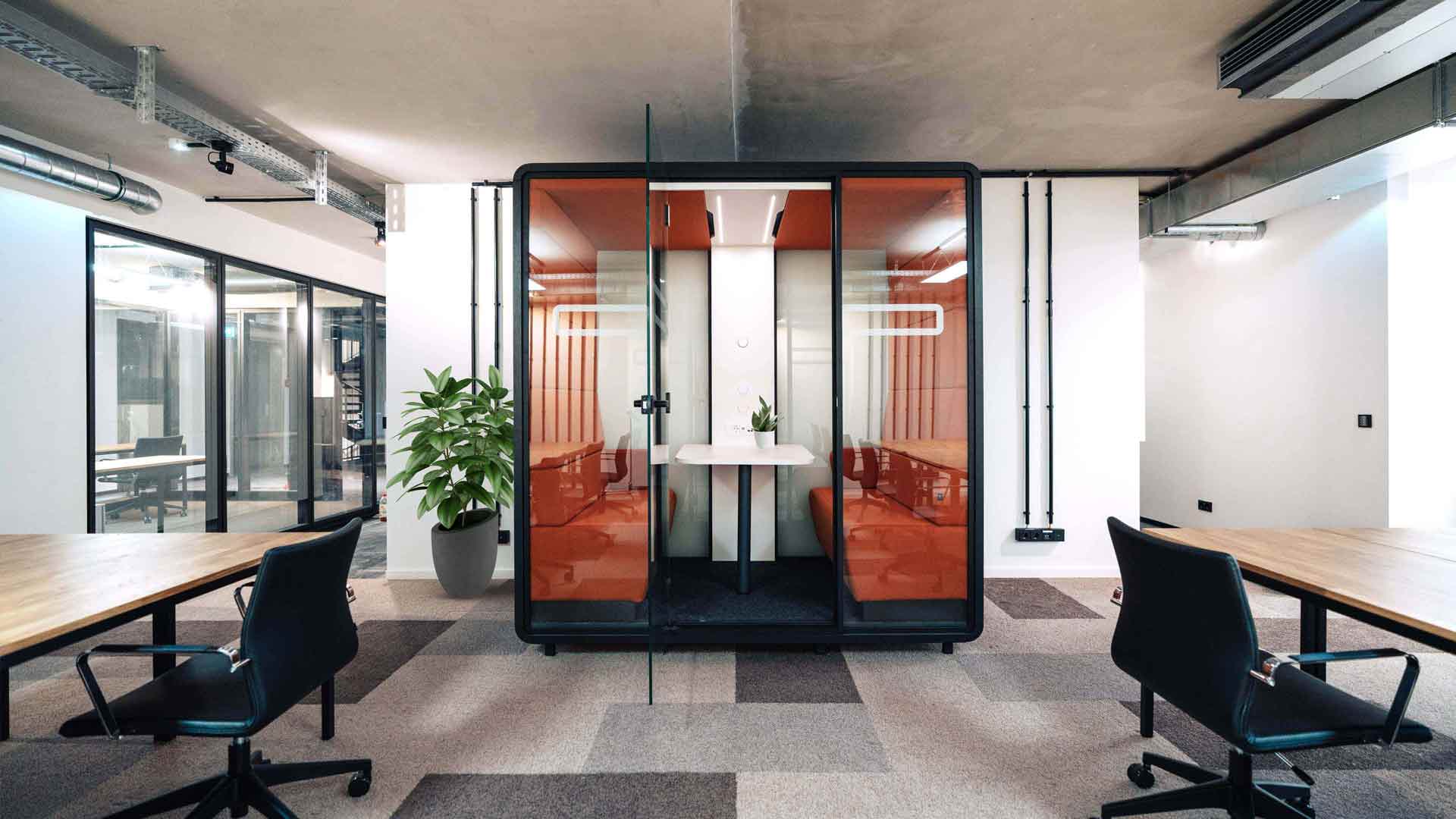 Bright Berlin coworking space at Pressehaus Podium with an orange glass meeting pod, wood desks, black chairs and a potted plant