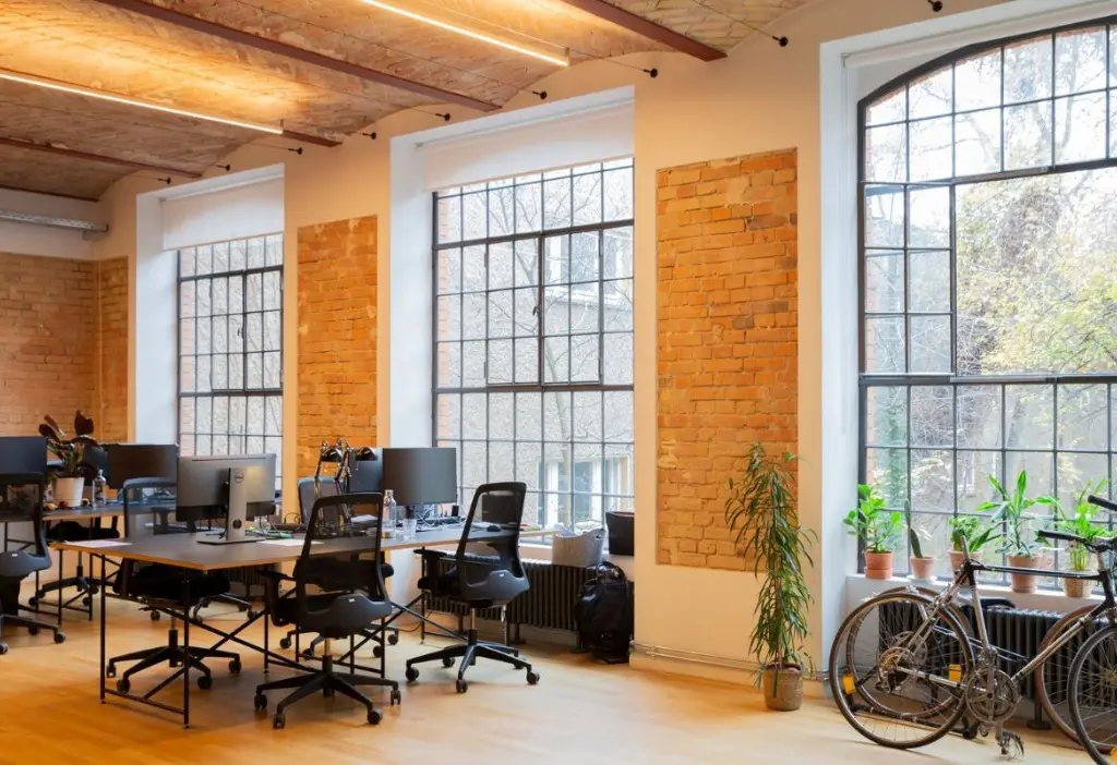 Industrious Berlin coworking space with exposed brick walls, tall arched windows, rows of desks and a bicycle by the window