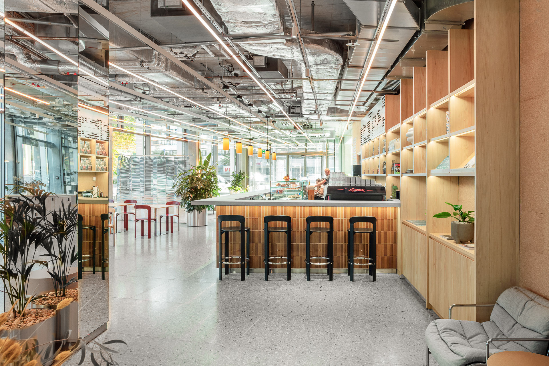 Mindspace Zimmerstraße cafe-style coworking area in Berlin with a wood bar, red and black stools, terrazzo floor and greenery