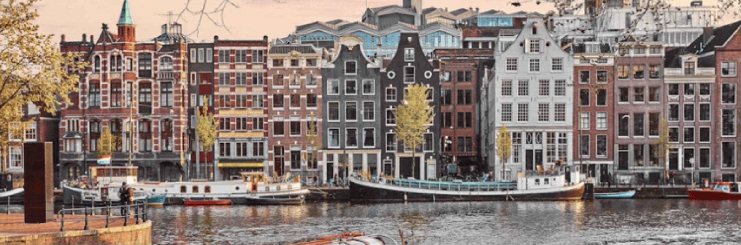 Amsterdam canal lined with colorful gabled Dutch townhouses and moored houseboats under a soft sky