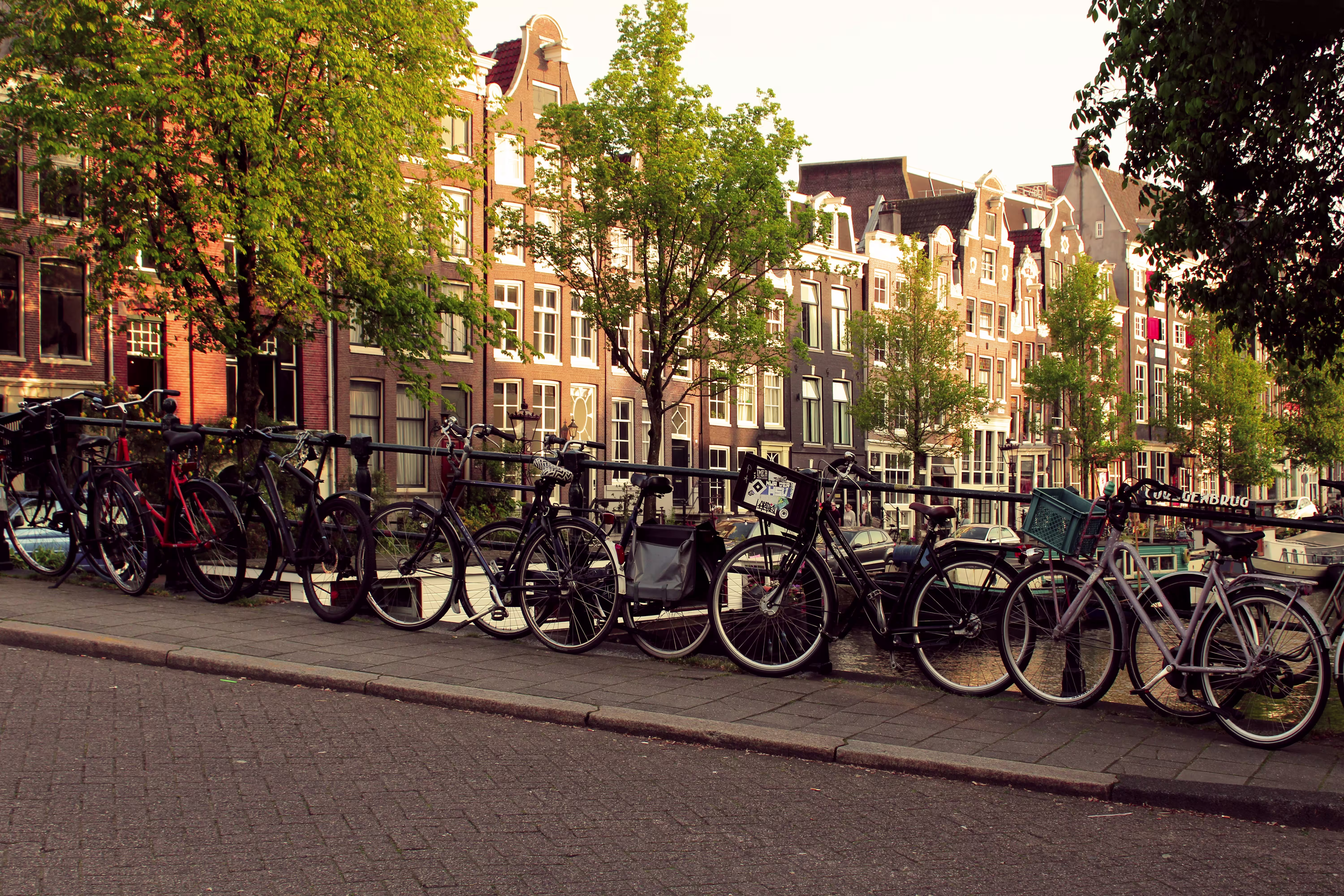Bicycles parked along an Amsterdam canal railing in front of traditional gabled townhouses