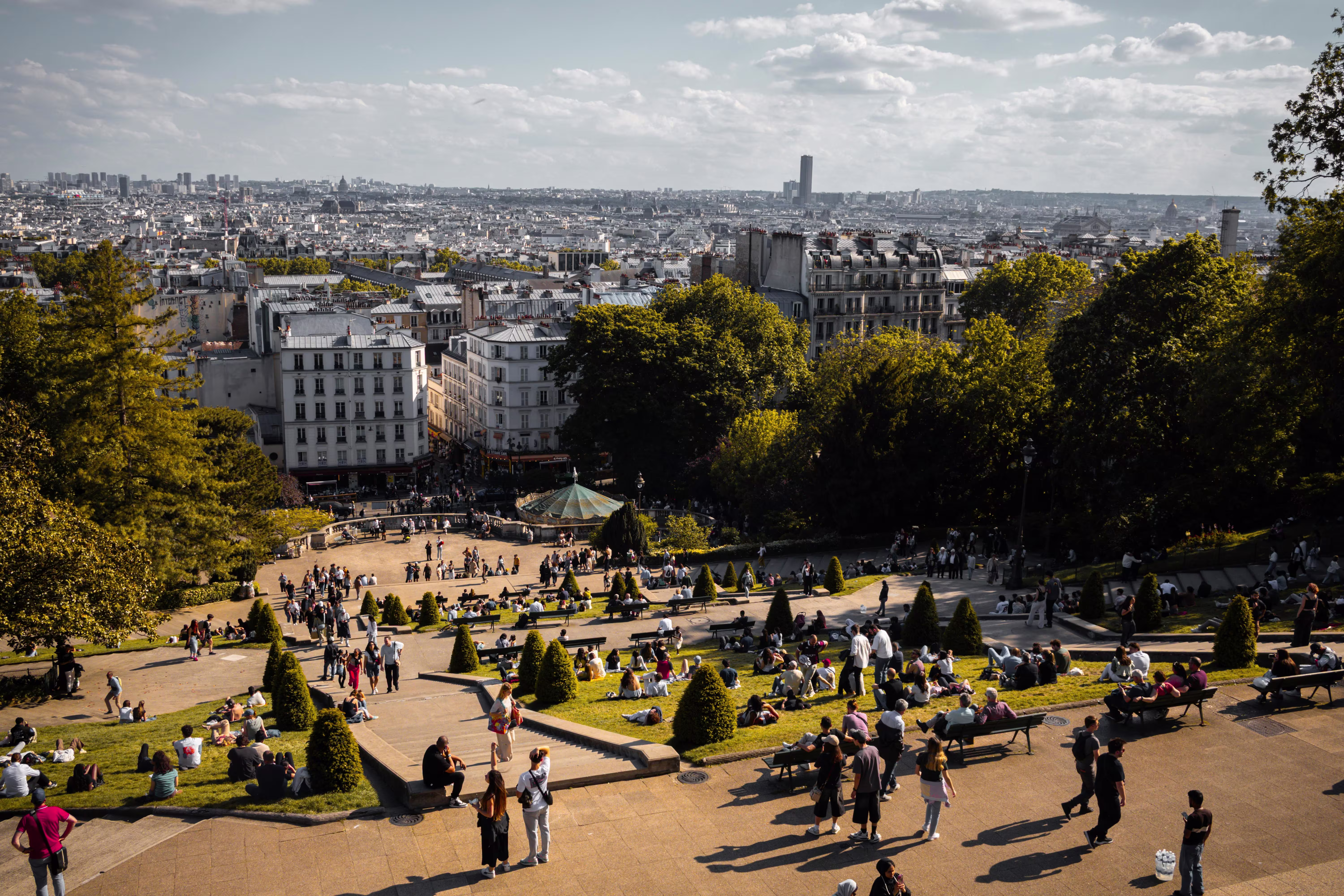 Summer view over Paris rooftops from Montmartre, with crowds relaxing on the park lawns and terraces below