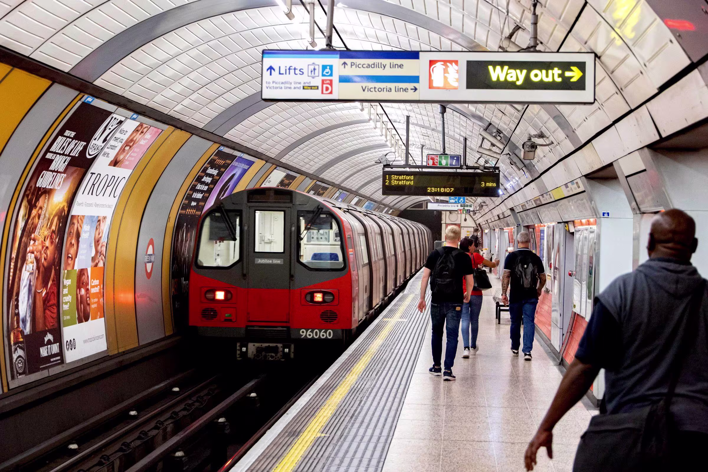 London Underground platform with a Tube train arriving, Way Out and line signs overhead and passengers walking