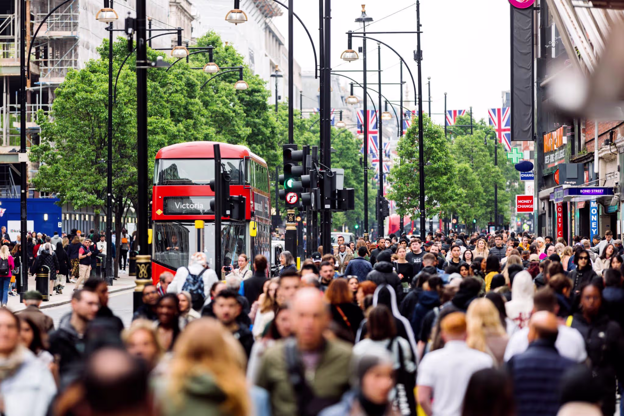 Crowded Oxford Street in London with a red double-decker bus, Union Jack flags and dense pedestrian traffic