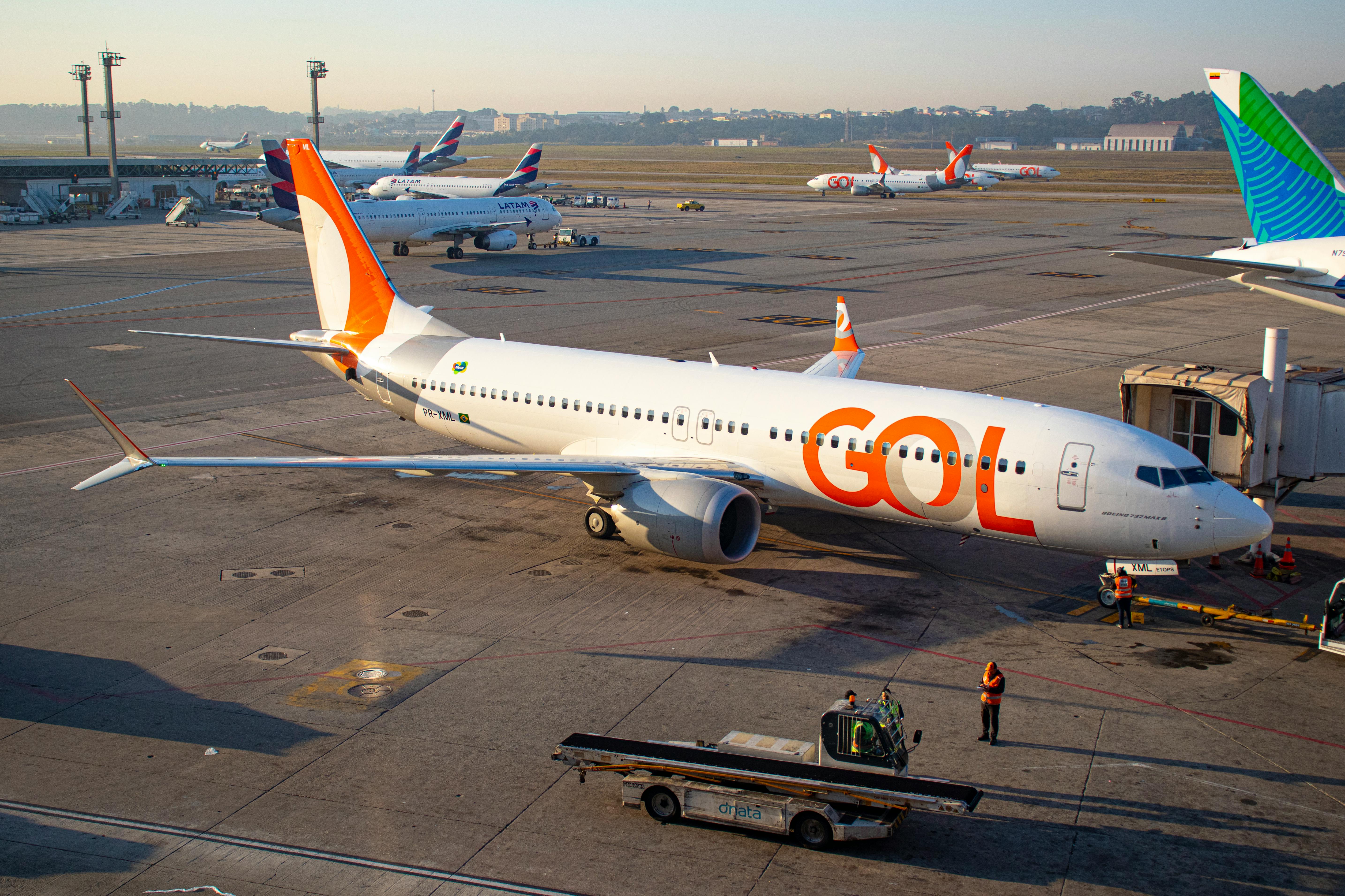 GOL Boeing 737 jet parked at a gate at Sao Paulo Guarulhos Airport with ground crew and baggage cart on the apron