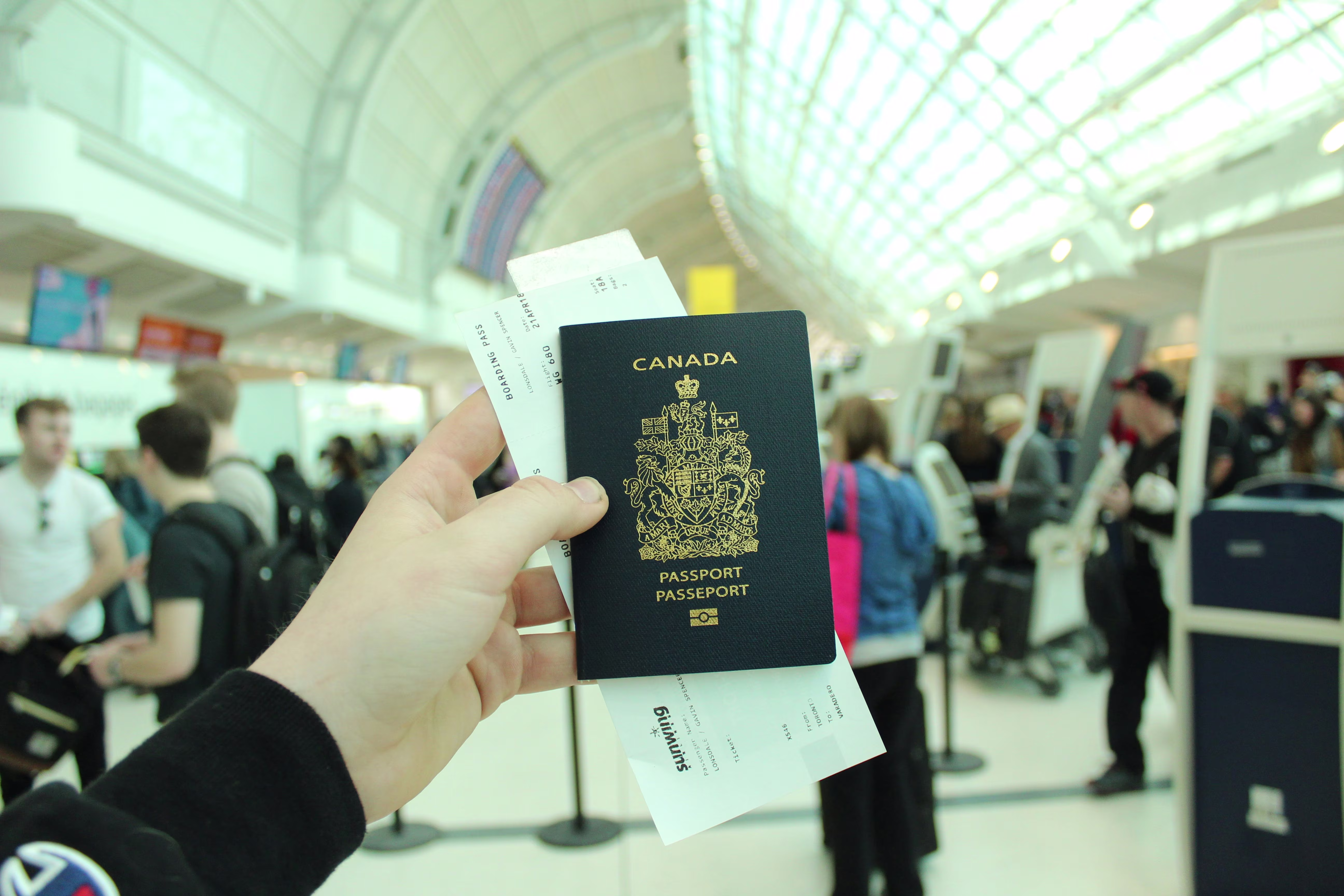 Traveler holding a Canadian passport and boarding pass at a busy airport check-in hall