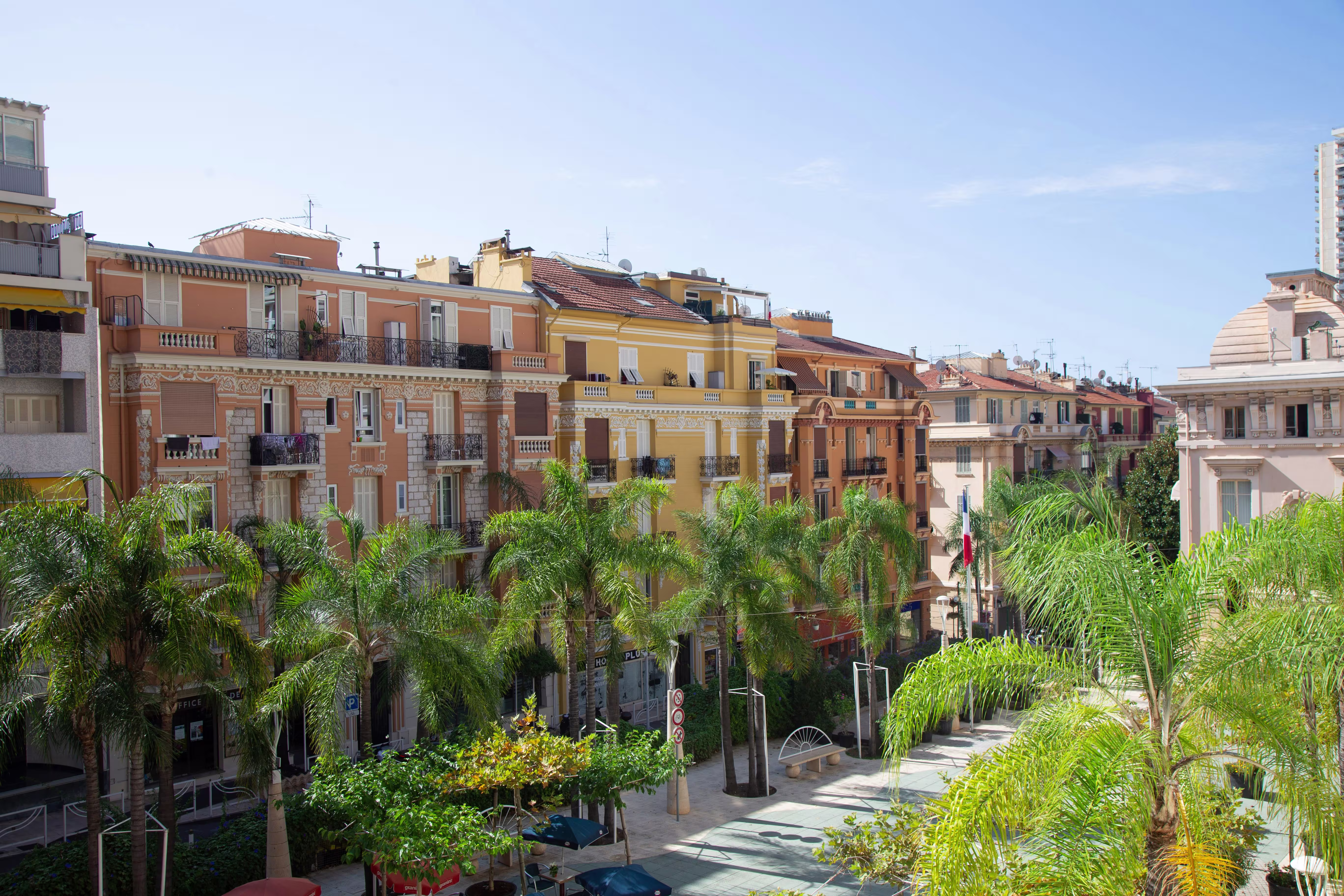 Beausoleil street near the Monaco circuit: rows of pastel Belle Epoque apartment buildings lining a palm-fringed plaza under blue sky