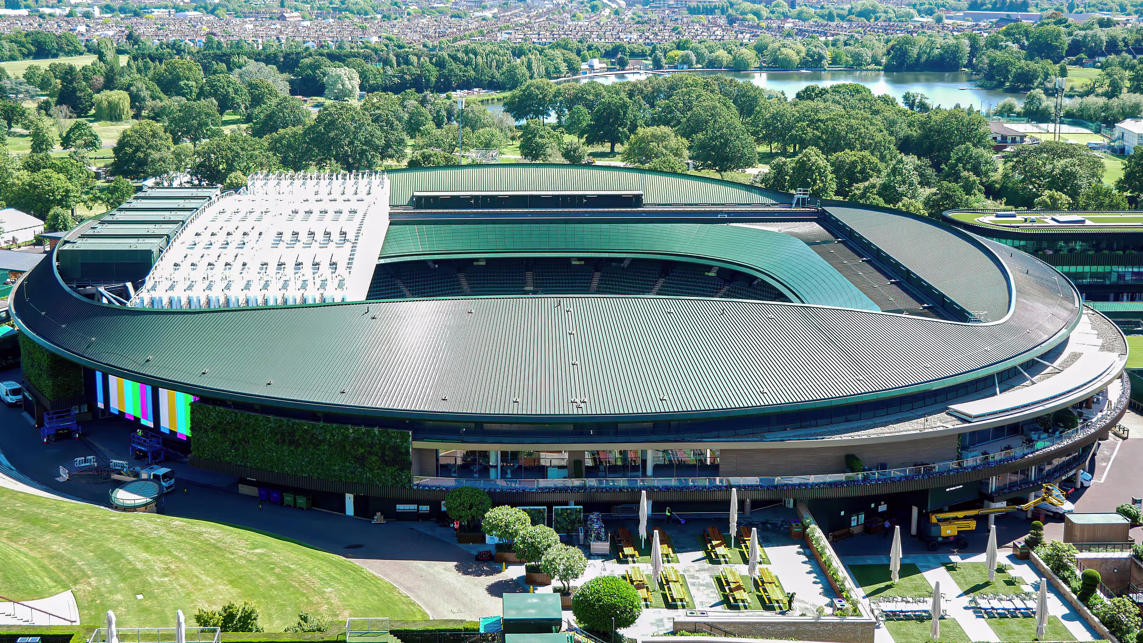 Aerial view of a tennis show court stadium at the All England Club, Wimbledon, ringed by green parkland and a lake